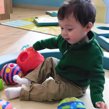 little boy sitting on classroom rug playing with toys